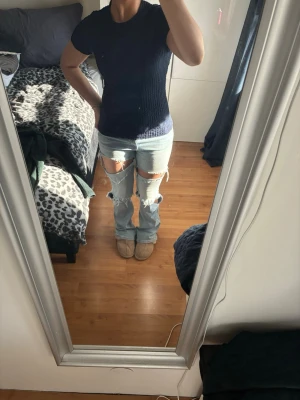 Svart ribbad topp med kort ärm - Säljer en svart topp med ribbad struktur och rund hals. Toppen har korta ärmar och är tillverkad i ett mjukt, stretchigt material som ger en skön passform. Perfekt för dig som gillar enkel och stilren design med lite extra textur.