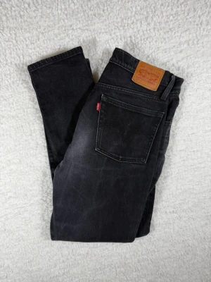 Svarta Levi's 501 jeans - Säljer ett par klassiska svarta Levi's 501 jeans med raka ben och fem fickor. Jeansen har en vintage look med diskreta slitningar och den ikoniska läderlappen bak i midjan. Tillverkade i bomull med knappgylf och snygga koppardetaljer.