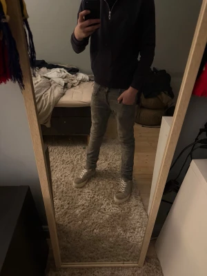 Grå slim fit jeans med slitningar - Säljer ett par grå slim fit jeans med snygga slitningar och tvättade detaljer. Jeansen har klassisk femficksmodell och smal passform som sitter tajt längs benen. Perfekta för en avslappnad och trendig look.