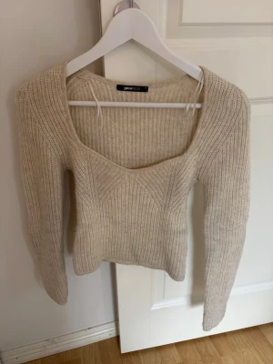 Beige ribbstickad tröja Gina Tricot - Trendig beige ribbstickad tröja från Gina Tricot med djup fyrkantig ringning och långa ärmar. Figurnära passform och mjukt material som ger en snygg siluett. Perfekt att styla med jeans eller kjol för en cool vardagslook.
