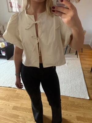 Vit blus med knyt från Gina Tricot - Supersöt vit blus från Gina Tricot med korta puffärmar och två knyt framtill. Blusen är croppad och har en luftig passform, perfekt till jeans eller kjol. 