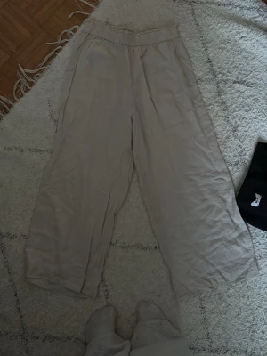 Beiga vida linnebyxor med resårmidja - Säljer ett par beiga linnebyxor med breda ben och resår i midjan. Byxorna har en bakficka och är gjorda i ett luftigt linnematerial, perfekta för en avslappnad och stilren look. Det passar perfekt för kortare människor🥰🥰