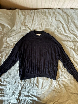 Svart stickad tröja Pernilla Wahlgren - En svart stickad tröja från Pernilla Wahlgrens kollektion, med ribbad rund hals och diskret strukturmönster. Tröjan har långa ärmar och är gjord i ett mjukt material som passar perfekt för att hålla dig varm under kyliga dagar. Enkel och stilren design.