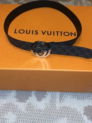 Svart Gucci bälte med GG-spänne - Snyggt svart bälte från Gucci med klassiskt GG-mönster och ett stort silverfärgat GG-spänne. Perfekt accessoar för att lyfta din outfit med en lyxig touch. Bältet är gjort i skinn och har en stilren design.