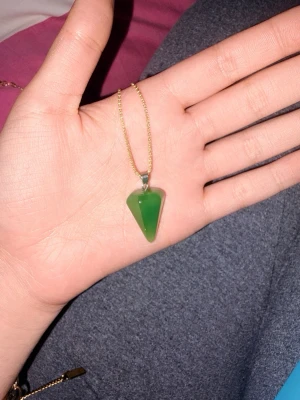 Halsband med grön sten - Snyggt halsband med en grön, konformad sten som hänge och tunn guldfärgad kedja. Perfekt för dig som gillar unika smycken med kristallkänsla. Kedjan är enkel och stilren vilket gör att hänget verkligen står ut.