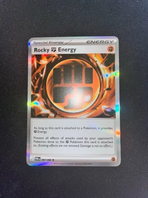 Pokémonkort Rocky Energy holo - Säljer ett Pokémonkort, Rocky Energy, med holoeffekt. Kortet har en cool design med orange och svart färgtema och är en specialenergi till Pokémon TCG. Perfekt för samlare eller spelare som vill boosta sin lek. Inga skador