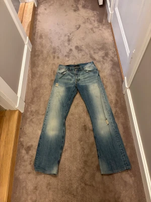 Ljusblå jeans från Nudie Jeans - Säljer ett par ljusblå jeans från Nudie Jeans med klassisk femficksdesign och orangea sömmar. Jeansen har slitna detaljer och raka ben. Materialet är 100% bomull och de har en snygg tvättad look. 31/34 storlek