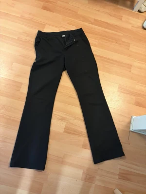 Svarta kostymbyxor med bootcut - Snygga svarta kostymbyxor med klassisk rak passform och pressveck. Byxorna har hällor för skärp, två sidofickor fram och två passpoalfickor bak. Perfekta för en stilren look. Materialet känns mjukt och följsamt.