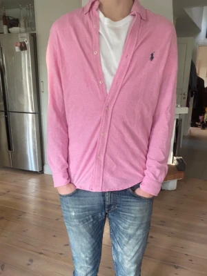Rosa skjorta från Ralph Lauren S - Snygg rosa skjorta från Ralph Lauren med klassisk krage och knappar framtill. Skjortan har lång ärm och en broderad logga på bröstet. Perfekt för en avslappnad men ändå stilren look. Skjortan är i 100% cottom 