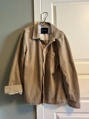 Beige manchester overshirt Lindbergh - Stilren beige overshirt från Lindbergh i mjuk manchester. Klassisk krage, bröstficka och knäppning framtill. Perfekt lager-på-lager-plagg med avslappnad passform och långa ärmar. Snygg att bära öppen eller stängd.