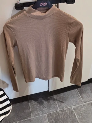 Beige ribbad polotopp från 157 - Säljer en beige ribbad polotopp från 157 i storlek S. Toppen har lång ärm och en hög krage, perfekt för lager-på-lager. Materialet är mjukt och stretchigt för en bekväm passform.
