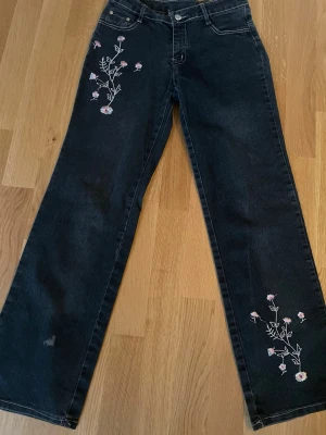 Marinblå med blommig brodyr - Coola blå jeans med raka utsvängda ben och broderade blommor framtill och på bakfickorna. 