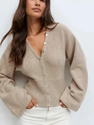 Beige ribbad kofta med v-ringning - Trendig beige kofta med v-ringning och knappar framtill. Koftan har vida ärmar och ribbad midja som ger en snygg siluett. Perfekt att matcha med jeans eller kjol för en avslappnad look.