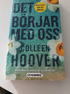 Det börjar med oss av Colleen Hoover - En gripande roman av Colleen Hoover, 'Det börjar med oss', i pocketformat. Omslaget är turkost med vita och orange blommor och tydlig text. Boken är en uppföljare till 'Det slutar med oss' och handlar om kärlek, relationer och nya början.