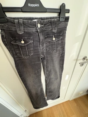 Grå jeans med fickdetaljer Gina tricot - Snygga grå jeans från Gina tricot  med raka ben och coola fickor framtill med lock och knapp. Jeansen har breda hällor och klassisk femficksdesign. Perfekta för en avslappnad och trendig look.
