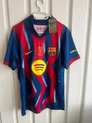 FC Barcelona matchtröja Nike blå/röd - Säljer en FC Barcelona matchtröja från Nike i blått och rött med gula detaljer. Tröjan har klubbmärke, sponsorlogga och Supercopa-emblem framtill samt namn och nummer 'ROONY 19' på ryggen. Tillverkad i lätt och ventilerande material, perfekt för fotboll.