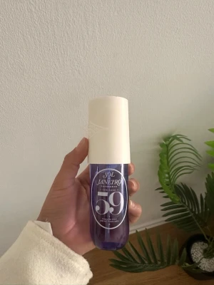 Sol de Janeiro 59 Parfymmist - En snygg parfymmist från Sol de Janeiro, doft 59. Flaskan är lila med en stor vit kork och har en modern, rundad form. Perfekt att ha med i väskan för en fräsch doftboost när som helst.