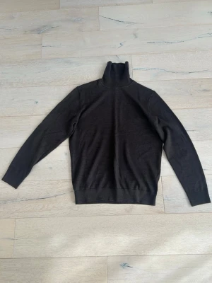 Brun polotröja från John Henric - Mörkbrun stickad polotröja från John Henric. Tröjan har lång ärm, hög polokrage och är tillverkad i ett tunt, mjukt material som passar perfekt till lager-på-lager. Klassisk och stilren modell.