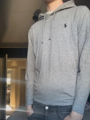 Grå hoodie från Ralph Lauren - Snygg grå hoodie från Ralph Lauren med klassisk huva och dragsnören. Tröjan har lång ärm och den ikoniska lilla loggan broderad på bröstet. Perfekt för en chill och stilren look. Mjuk bomullskänsla och enkel att matcha med jeans eller joggers. Pris är diskuterbart