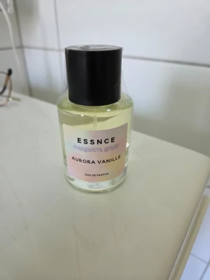 Aurora Vanille parfym från Essnce, Helt ny! - Helt oöppnad Aurora Vanille Eau de Parfum från Essnce, designad av Margareta Gräs. Flaskan är genomskinlig med ljusgul vätska och har en svart rund kork. Etiketten är ljusrosa med svart text. Perfekt för dig som gillar söta och mjuka dofter.