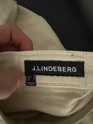 Beiga chinos från J.Lindeberg - Snygga beiga chinos från J.Lindeberg i klassisk rak modell. Byxorna har en stilren look och är tillverkade i ett mjukt bomullstyg. Perfekta för dig som vill ha en clean och modern stil. Storlek 29/32.