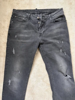 Grå slitna jeans från Dsquared2, oanvänd - Säljer ett par grå jeans från Dsquared2 med snygga slitningar och hål på flera ställen. Jeansen har fem fickor, knappgylf och klassisk passform. Materialet är denim och de har en cool, lite tvättad look.