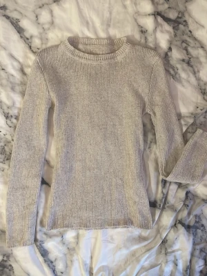 Beige ribbstickad tröja one size - Säljer en beige ribbstickad tröja med rund hals och långa ärmar. Tröjan är i ett mjukt material och har en enkel, stilren design som passar till det mesta. Perfekt för lager-på-lager och enkel att matcha med andra plagg.