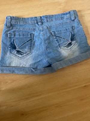 Blå jeansshorts från Sweet Jeans - Snygga blå jeansshorts från Sweet Jeans med uppvikta benslut och dekorativa bakfickor med broderi och nitar. De är 42 i midjan och hella shortsen är ca 28 lång ❤️står ej storlek me. Skulle gissa på 38-40