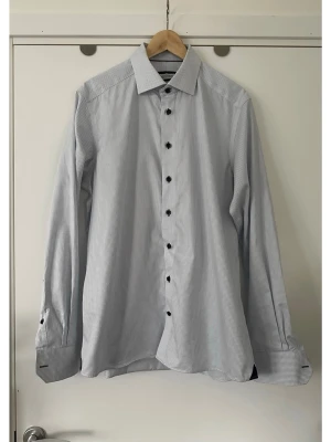 Ljusblå rutig skjorta från J. Harvest & Frost - Skräddarsydd ljusblå skjorta från J. Harvest & Frost i storlek L / 41/42. Slim fit. Klassisk modell med lång ärm och krage och svarta knappar framtill och vid ärmsluten. Diskret rutigt mönster över hela tyget, och kul isydda detaljer i kontrastfärg vid knäppning och ärmslut. 100% bomull, så bra material som andas. Välsydd kvalitetsskjorta. Mycket gott skick, som ny. Nypris 1399:-.  Skickas mot porto, kan även hämtas i Stockholm.