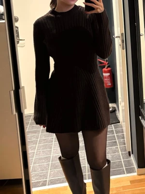 Mörk ribbad stickad klänning - Säljer en mörk, ribbad stickad klän sopassad med lång ärm och rund hals. Klänningen är kort och har en loose passform som ger en avslappnad men ändå stilren look. Perfekt att matcha med boots och strumpbyxor.