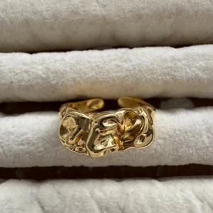 Guldfärgad ring - Säljer en unik guldfärgad ring med en cool, abstrakt design. Ringen har en skulpterad yta som ger den ett konstnärligt och modernt utseende. Perfekt för att ge din outfit en extra touch av stil!