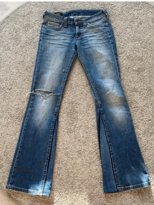 Blå bootcut jeans från Lee - Säljer ett par blå bootcut jeans från Lee med slitningar och hål på vänster lår. Jeansen är låg midjade och är tillverkade i denim med lätt stretch. Perfekta för en avslappnad och trendig look. De är omsydda där nere och det finns lite små hål och om ni vill ha mer bilder skriv gärna!!❤️ (bilder från en annan säljare) 