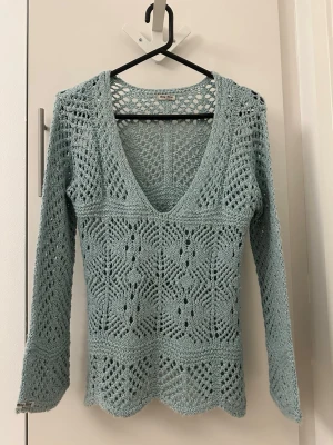 Ljusblå virkad tröja från Miu Miu - Supersnygg ljusblå stickad tröja från Miu Miu med djup V-ringning och lång ärm. Tröjan är virkad i ett genombrutet mönster och har vågig nederkant. Perfekt för lager på lager och ger en cool vintage vibe.