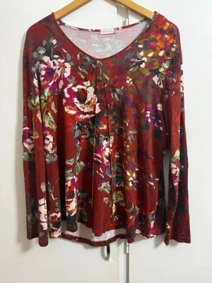 Blommig långärmad topp från Ted Nicol - Snygg långärmad topp från Ted Nicol  i röd bas med färgstarkt blommigt mönster. Toppen har rund halsringning och är tillverkad i ett mjukt och stretchigt material som sitter bekvämt. Perfekt för dig som gillar färg och mönster.