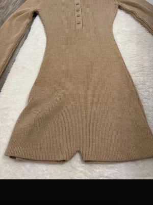 Beige ribbad jumpsuit med krage - Säljer en beige ribbad jumpsuit från mango med lång ärm, krage och knappar framtill. Materialet är stretchigt och mjukt, perfekt för en trendig och bekväm look. Snygg passform som framhäver figuren och ger en stilren vibe.