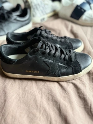 Svarta Golden Goose sneakers - Svarta sneakers från Golden Goose med vit sula, svart stjärndetalj på sidan och texten GGDB/STAR i guld. Skorna har svarta skosnören och mockadetaljer vid hälen där det står GOLDEN GOOSE. Klassisk låg modell i läder och mocka. (Ingen låda till) 