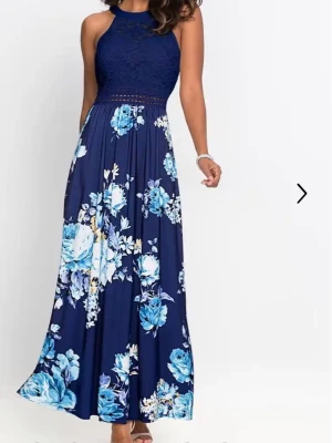 Marinblå långklänning med spets och blommor  - Säljer en marinblå långklänning med spetsliv och blommigt mönster i blått och vitt. Klänningen har ärmlös design, hög halsringning och ett fallande kjolparti i mjukt material. Perfekt för sommarens alla tillfällen! Aldrig använd. 