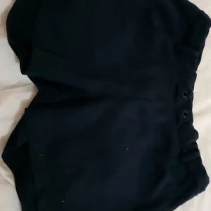 Svarta shorts från Name It - Svarta shorts från Name It med hög midja och enkel design. Tillverkade i mjukt material som passar perfekt till sommaren. Klassisk look utan synliga detaljer förutom diskreta öljetter vid midjan.