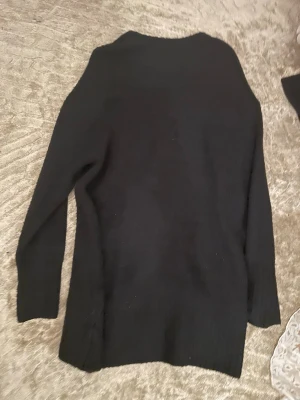 Svart stickad tröja med lång ärm - En enkel svart stickad klänning med lång ärm och rak passform. Materialet känns mjukt och bekvämt mot huden. 