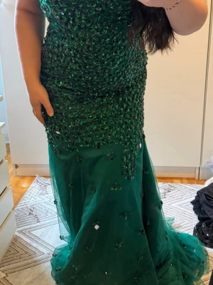 Grön exklusiv långklänning med paljetter - Säljer en fantastisk grön långklänning med massor av glittrande paljetter och stenar upptill. Klänningen har en figurnära passform upptill och faller snyggt ner mot golvet. Perfekt för bal eller fest. Materialet känns lyxigt och skimrande.