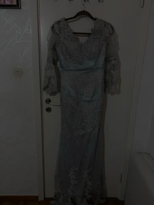 Ljusblå långklänning med spetsdetaljer - Elegant ljusblå långklänning med v-ringning och vackra spetsdetaljer över hela klänningen. Klänningen har trekvartsärm i spets och markerad midja. Perfekt för speciella tillfällen och har en romantisk känsla. Ser inte ut som på bild sitter jätte fint på 