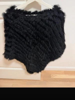 Svart pälsväst i äkta päls - Snygg svart pälsväst i mjuk päls med fluffig känsla och kortare modell. Västen har en stilren design utan synliga knappar eller dragkedja och passar perfekt för att lyfta en outfit. Perfekt för dig som gillar trendiga och mysiga plagg.