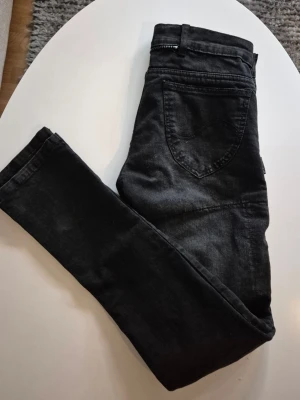 Svart/grå kevlarjeans * stl S/M * Flying Eagle - * Svart/grå kevlarbyxor från FlyingEagle. * Märkta stl 38. Se måtten nedan. * Fickor för höft och knäskydd. * Dragkedja bak för att kunna fästa ihop med jacka. * Stängs med knapp & dragkedja. * Står 100% bomull och kevlar, men jag tycker att de är lite stretchiga. * Midjemått mätt rakt över: ca 80 cm. * Mått innerben: ca 82 cm * Total längd: ca 109 cm * Jättebra skick. Hittar inga skavanker.  Djur och rökfritt hem. Se bilder och förstora då de ingår i beskrivningen.