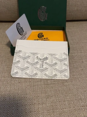 Vit kortfodral från Goy4ard - Snyggt vitt kortfodral från Goy4ard med det klassiska mönstret och loggan framtill. Tillverkat i exklusivt läder med flera fack för kort. Perfekt för dig som vill ha en stilren och lyxig accessoar i fickan.