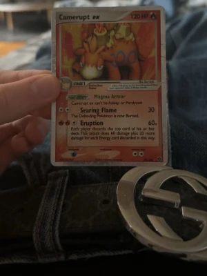 Camerupt ex Pokémonkort - Camerupt ex Pokémonkort med 120 HP från EX-serien. Kortet har en röd-orange bakgrund och visar Camerupt med eld och lava. Text och attacker som Magma Armor, Searing Flame och Eruption finns på kortet. Perfekt för samlare eller Pokémonfans.