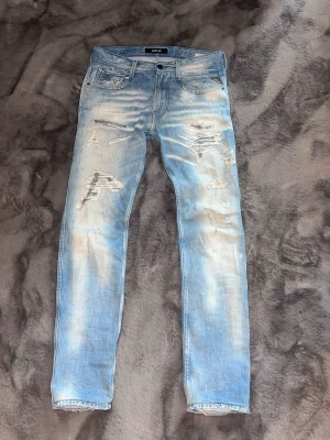 Replay anbass med slitningar  - Säljer ett par ljusblå jeans från replay med slitningar och distressed detaljer på både fram- och baksida. Dom öron modellen anbass vilket är slim fit. Sjukt snygg tvätt och perfekta för varmare dagar