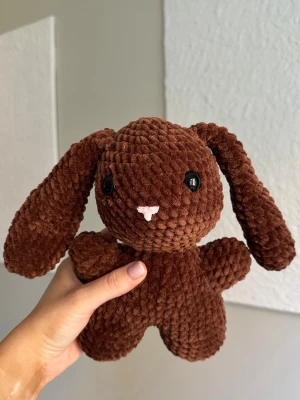 Brun virkad kanin - Virkat gosedjur i velvetgarn. Kaninen är 26cm lång och tillverkad för hand, vilket gör varje kanin unik. Kaninen har svarta säkerhetsögon som sitter fast från insidan. Rekommenderas dock inte för de allra minsta barnen, då det alltid finns en viss risk, vid hårt drag, att de lossnar. Perfekt som present eller mysig inredningsdetalj! Tvättråd: max 30°C, handtvätt.