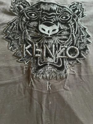 Svart Kenzo t-shirt med tigerbrodyr - Snygg svart t-shirt från Kenzo med ikonisk tigerbrodyr och texten 'Kenzo Paris' framtill. Klassisk passform och rund halsringning. Perfekt för dig som vill sticka ut med en stilren och trendig look. Str S