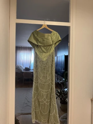 Klänning Ljusgrön  med paljetter - Elegant ljusgrön långklänning i satin med vacker paljettbrodyr. Jag har endast använt den en gång och ny köpt. Den är i väldigt ny och bra skick!, passformen ser ut såsom på andra bilden. Passar för storlekar XS/S. Priset är mycket lägre än original priset, men kan diskuteras.