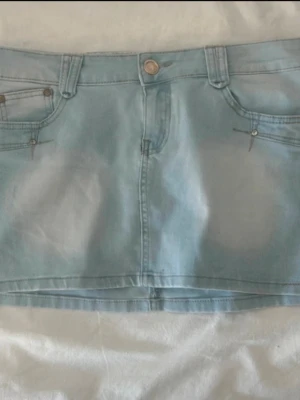Ljusblå jeanskjol Lågmidjad  - Snygg ljusblå jeanskjol från Jeanswest med klassisk femficksdesign, bälteshällor och knappstängning. Kjolen är kort och har en enkel, rak passform som passar perfekt till en avslappnad stil.